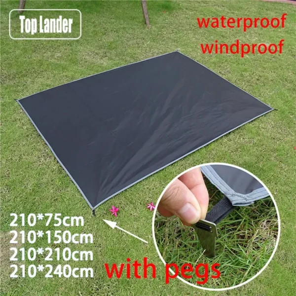 Grey waterproof picnic mat with pegs staked at each corner on grass beside a camping tent