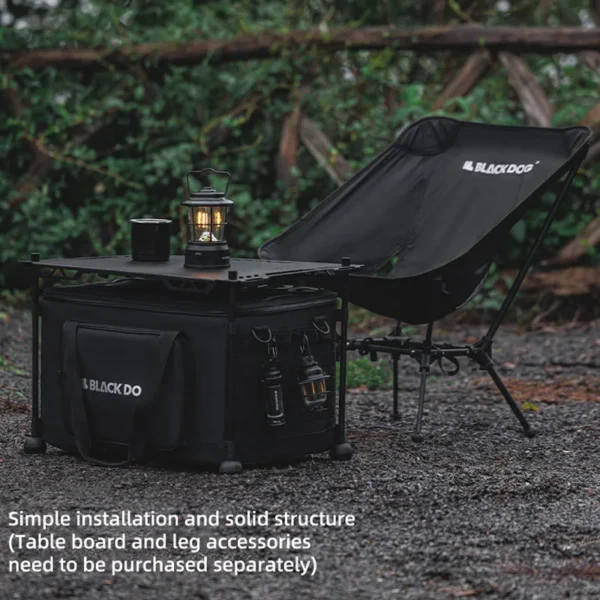 Black collapsible sundries storage bag with side opening and zippered side pockets at a campsite