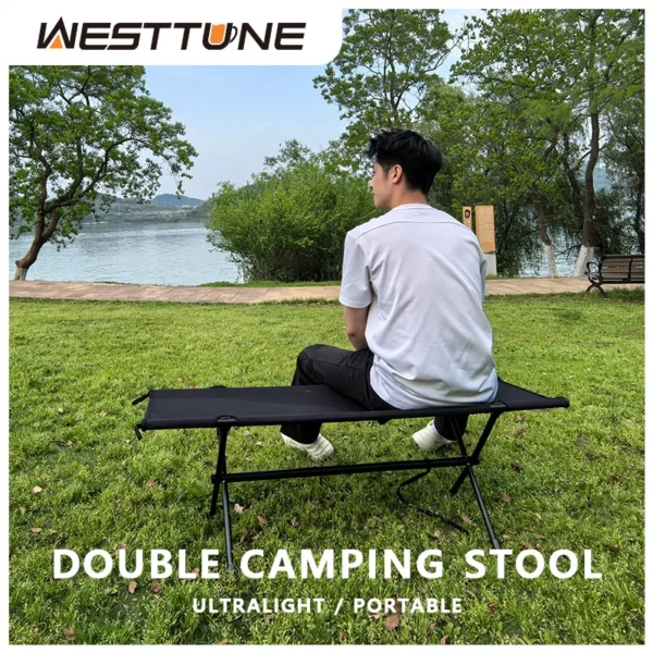 Two person camping bench with khaki fabric seat and aluminum legs set up at a campsite