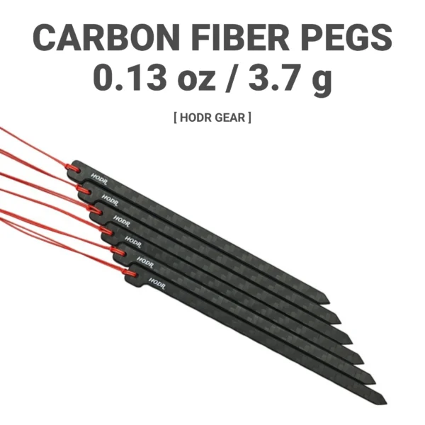 Carbon fiber tent stakes in matte black with red pull cords laid beside a DCF storage bag