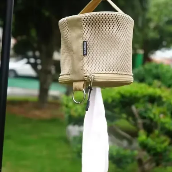 Camping toilet paper holder in khaki hanging from a tree branch near a tent