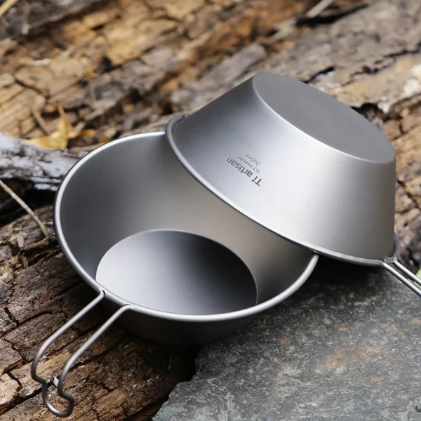 Titanium camping bowl in sierra cup style with fixed handle on a camp table